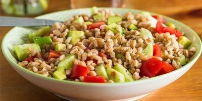White bowl filled with farro, chunks of cucumber and tomato.